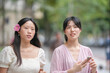 © Masakazu Tokashiki - Two women are walking down a street, one of them holding a cell phone. The other woman is wearing a pink flower in her hair. Scene is casual and relaxed