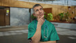 © Krakenimages.com - Caucasian male doctor in green uniform with stethoscope in an outdoor street setting, appearing deep in thought with a contemplative expression.