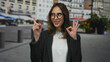 © Krakenimages.com - Woman wearing glasses smiling and gesturing okay sign on city street with urban buildings in the background.