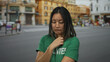 © Krakenimages.com - Woman in green volunteer t-shirt standing on city street with a concerned expression, reflecting urban life and youth involvement in outdoor volunteer activities.