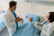 © Dorde - Senior Caucasian Woman Smiling in Hospital Bed with Medical Professionals Providing Care