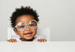 © Artem Zatsepilin - adorable african american baby with colorful glasses smiling against neutral background with copy space. healthcare awareness, pediatric care, national eye exam month poster