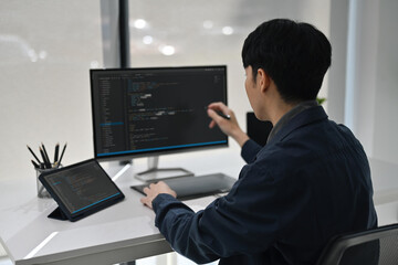 An Asian software developer focused on coding and digital tasks in a tech-friendly, modern office environment