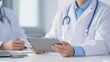 © 69 - Doctor in White Coat Using Tablet for Medical Consultation in Modern Healthcare Office with Another Medical Professional Present