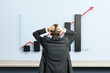 © Who is Danny - Businessman holding head in front of rising bar chart and red arrow on wall symbolizing financial growth and leadership stress in modern office room.