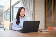 © matinee - Professional businesswoman working on a laptop at wooden desk in a modern office with natural light.