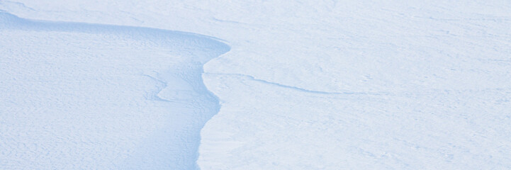 Wall Mural - Beautiful winter background with snowy ground. Natural snow texture. Wind sculpted patterns on snow surface. Wide panoramic texture for background and design.