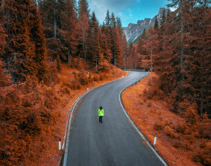 Wall Mural - aerial view of woman walking on a winding mountain road in red forest on autumn rainy day. dolomites