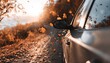 © oksa_studio - Fallen autumn leaves swirl around a car driving on a scenic road at sunset, creating a picturesque fall scene