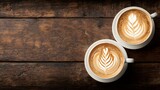 Two cups of cappuccino with latte art sit atop a rustic wooden surface, showcasing rich browns and creamy whites.