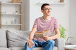© Pixel-Shot - Young man in eyeglasses reading book on sofa at home