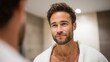 © SerPak - A man with a beard and short hair gazes at his reflection in a modern bathroom. The atmosphere is calm and introspective, ideal for wellness themes.