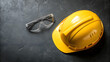 © gleb - Yellow construction hard hat and transparent protective safety glasses on dark textured concrete surface, essential equipment for workplace safety manuals and industrial training visuals