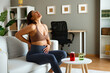 © djile - Pregnant woman holding her belly and touching her back, suffering from back pain while sitting on the sofa at home