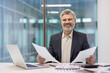 © Liubomir - Smiling business professional reviewing documents at a modern office desk.
