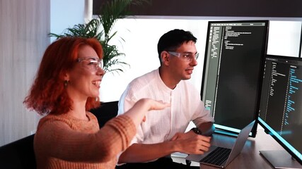 Asian female finance officer wearing glasses with a co-worker programmer discussing software writing. A coder or developer working in a computer display discussing problem solving.