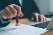 © Dilok - Businessman stamping approval on official document with laptop, legal contract validation certification agreement paperwork authorization business approval process and corporate compliance.