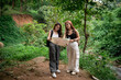 © WMSTUDIO - Two Young Women Exploring Nature While Holding a Map in a Lush Green Forest by a Stream on a Sunny Day