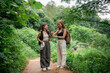 © WMSTUDIO - Two Smiling Friends Enjoying Nature Walk in Lush Green Forest Trail with Backpacks and Casual Clothing