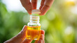 © SkNur - “Close-up Hand Holding Glass Bottle of Golden Essential Oil with Sunlight and Green Foliage Background – Macro Photography
