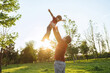 © Arsenii - Father tossing his smiling young son into the air and catching him while playing together outdoors in a sunny park at sunset. Space for text