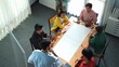 © InfiniteFlow - Top view of skilled manager discussing and explain strategy at meeting. Professional smart businessman standing at blackboard and sharing marketing plan while brainstorming idea at table. Convocation.