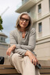 © Ivan Traimak - Woman in gray sweater sits on outdoor bench at modern building during cloudy day