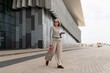 © Ivan Traimak - Woman walking in casual attire along a modern building in a coastal city at midday