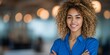 © Rifqi - Smiling black woman in a blue shirt with curly hair, arms crossed in an office setting, concept for corporate portrait, business leadership, and workplace diversity