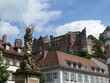 Golden statue of Virgin Mary with baby Jesus standing in front of Heidelberg Castle in Germany, with residential buildings in the foreground