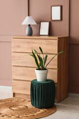 Poster - chest of drawers with lamp, blank frames and pouf near brown wall in room