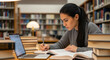 © ProArt Studios - Focused university student diligently writing in a textbook, simultaneously utilizing a laptop for research in a quiet academic library setting.