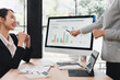 © kenchiro168 - Quarterly business growth performance presentation with colleagues discussing colorful bar chart on desktop monitor, collaborative office meeting conveying professional focus and optimism