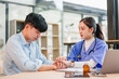 © kenchiro168 - Young patient and female medical professional holding hands in calm consultation, compassionate conversation in clinic setting with stethoscope and prescription bottle on desk