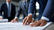 © Curioso.Photography - Group of businessmen in suits reviewing architectural blueprints or technical documents at a table.