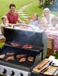 © Ilona - A family is gathered in a backyard celebrating with a barbecue. Grilled steaks sizzle on the grill while children and adults enjoy the meal and each other's company
