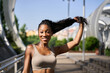 © Oscar - Young sporty black woman holding her long hair smiling in the city