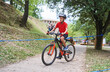 © Marc Elias - Determined boy in red shirt riding mountain bike on forest trail during outdoor cycling competition