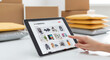 © Ruman - Photo of a persons finger points to a tablet displaying an ecommerce website with various products, surrounded by shipping packages and envelopes