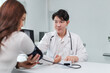 © amnaj - Asian male doctor using sphygmomanometer with stethoscope checking blood pressure of female patient in hospital or clinic