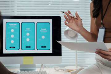 Wall Mural - web designer holding documents while pointing at a computer screen displaying a mobile app design, c