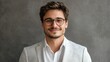 © Nany - A man with glasses and a beard, wearing a white shirt and a gray suit jacket, standing against a gray background with a neutral expression.