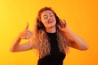 © New Africa - Happy woman listening to music in headphones and showing thumbs up on yellow background