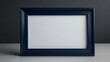 © Ridwan - Elegant navy blue wooden picture frame with a blank white mat, standing upright on a table against a dark wall, perfect for mockups and copy space