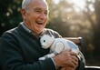 © Alper AI - An elderly man happily hugs a robotic cat, enjoying a sunny day outdoors.