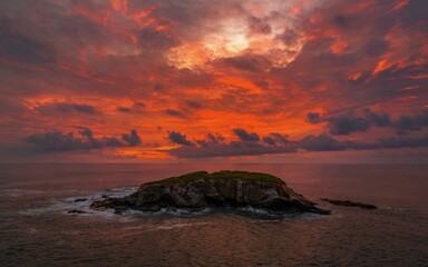 Wall Mural - Sunset over rocky island with vibrant sky.