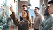 © Prostock-studio - Portrait of young businesswoman mentor coach leader writing idea or task pointing at sticky notes on glass wall, diverse team developing work plan in creative corporate office at stand up meeting