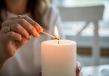 Fair skinned woman lights thick white candle with a match during an indoor scene