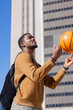 © Wavebreak Media - African american man in his twenties spinning orange basketball at city plaza, backpack