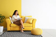 © Pixel-Shot - Young Asian woman reading magazine on yellow sofa near color wall